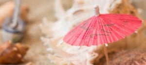 Red paper cocktail umbrella with seashells on sand